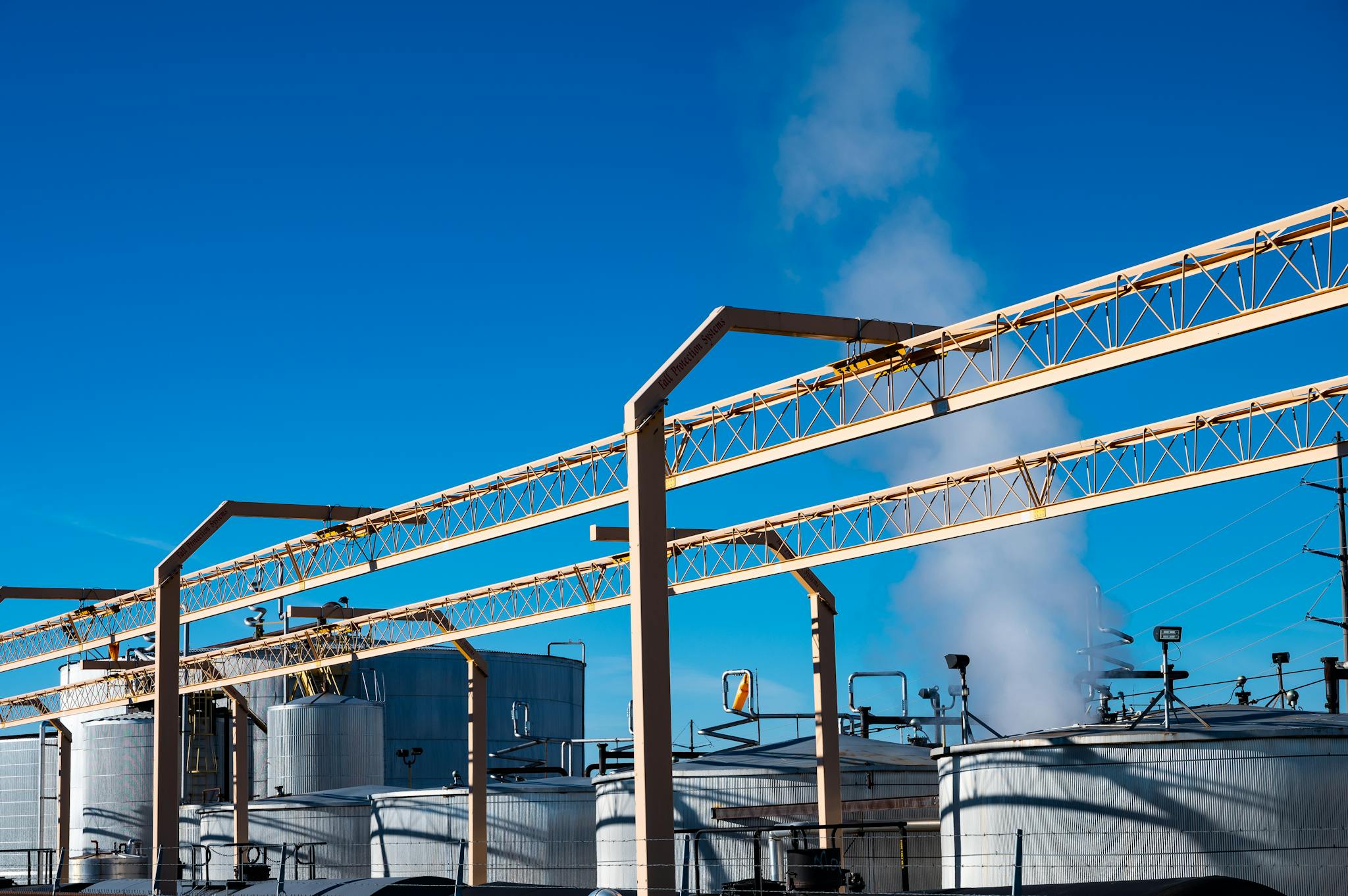 Wide view of an industrial plant with smoke rising from storage tanks against a clear blue sky.
